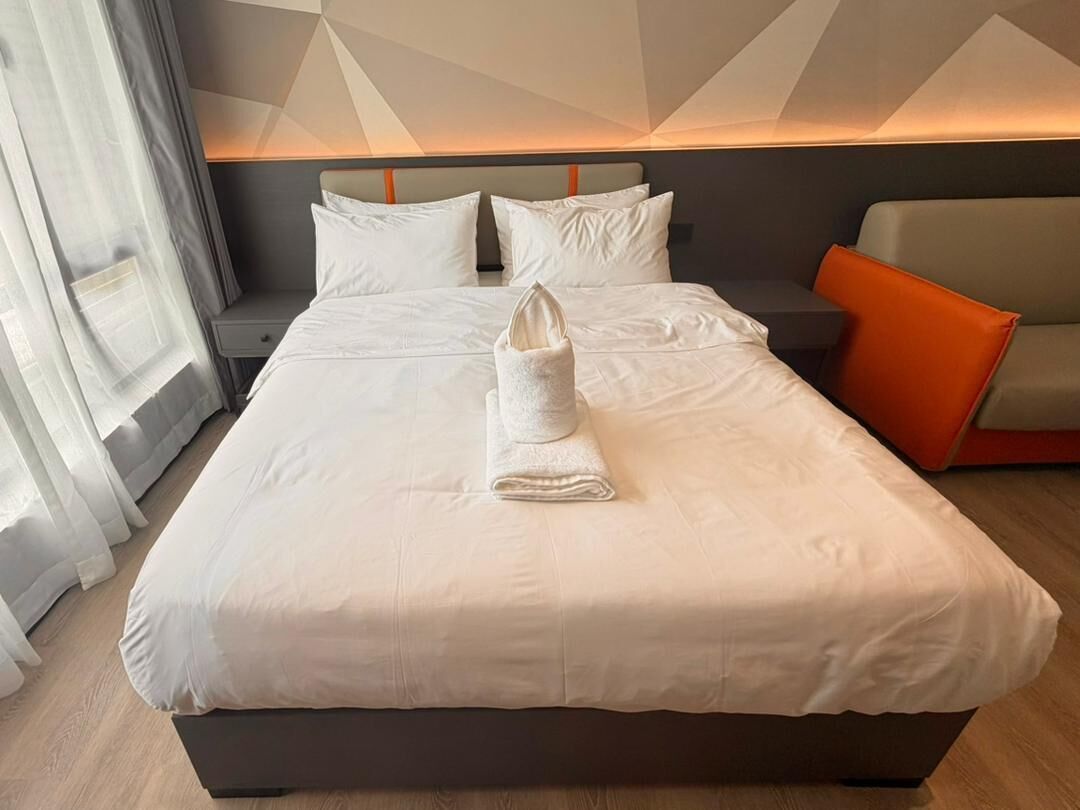 Habitación de hotel con una cama grande, una mesita de noche, un sofá y una ventana con cortinas.