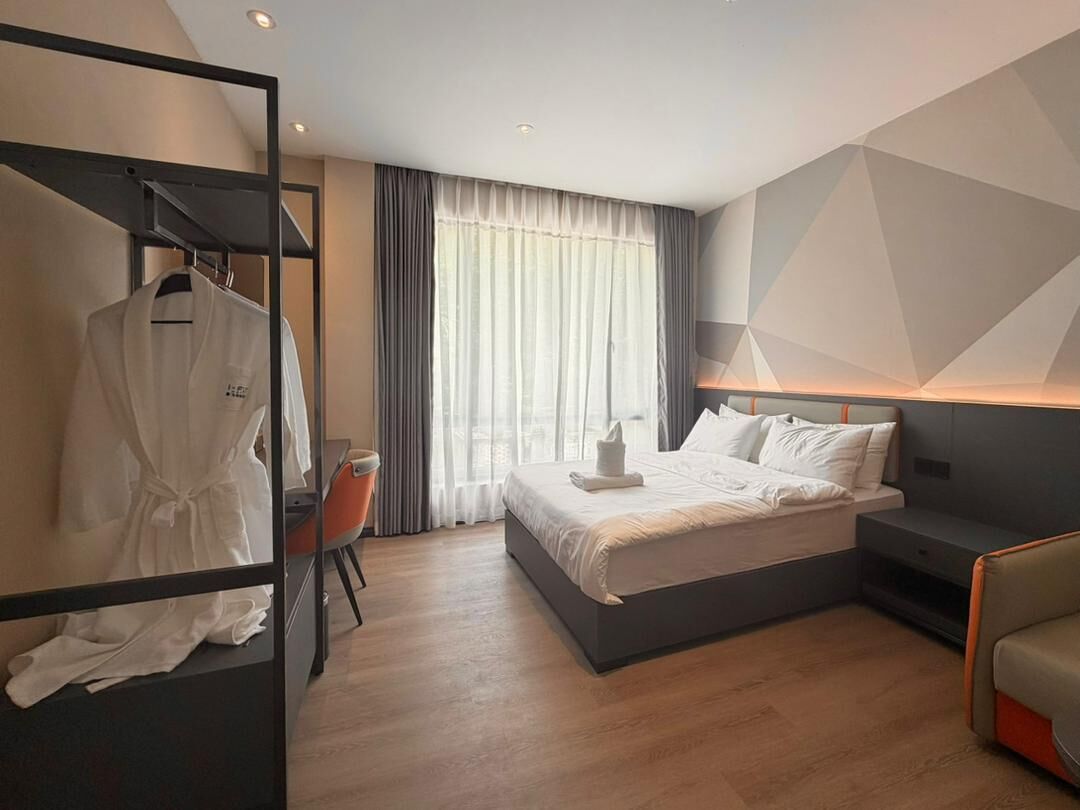 A modern hotel room with a bed, a seating area, a wardrobe, and a window with curtains.