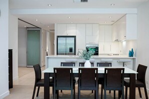 Une cuisine moderne avec des meubles blancs, un îlot central et un coin repas comprenant une table et des chaises.