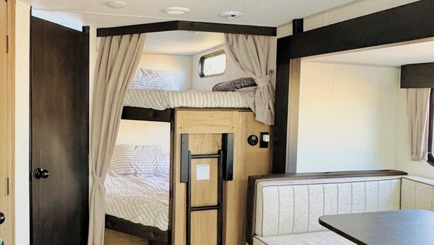 Ein kompakter Wohnraum in einem Wohnmobil mit Etagenbett, kleinem Fenster, Küchenzeile und Badezimmertür.