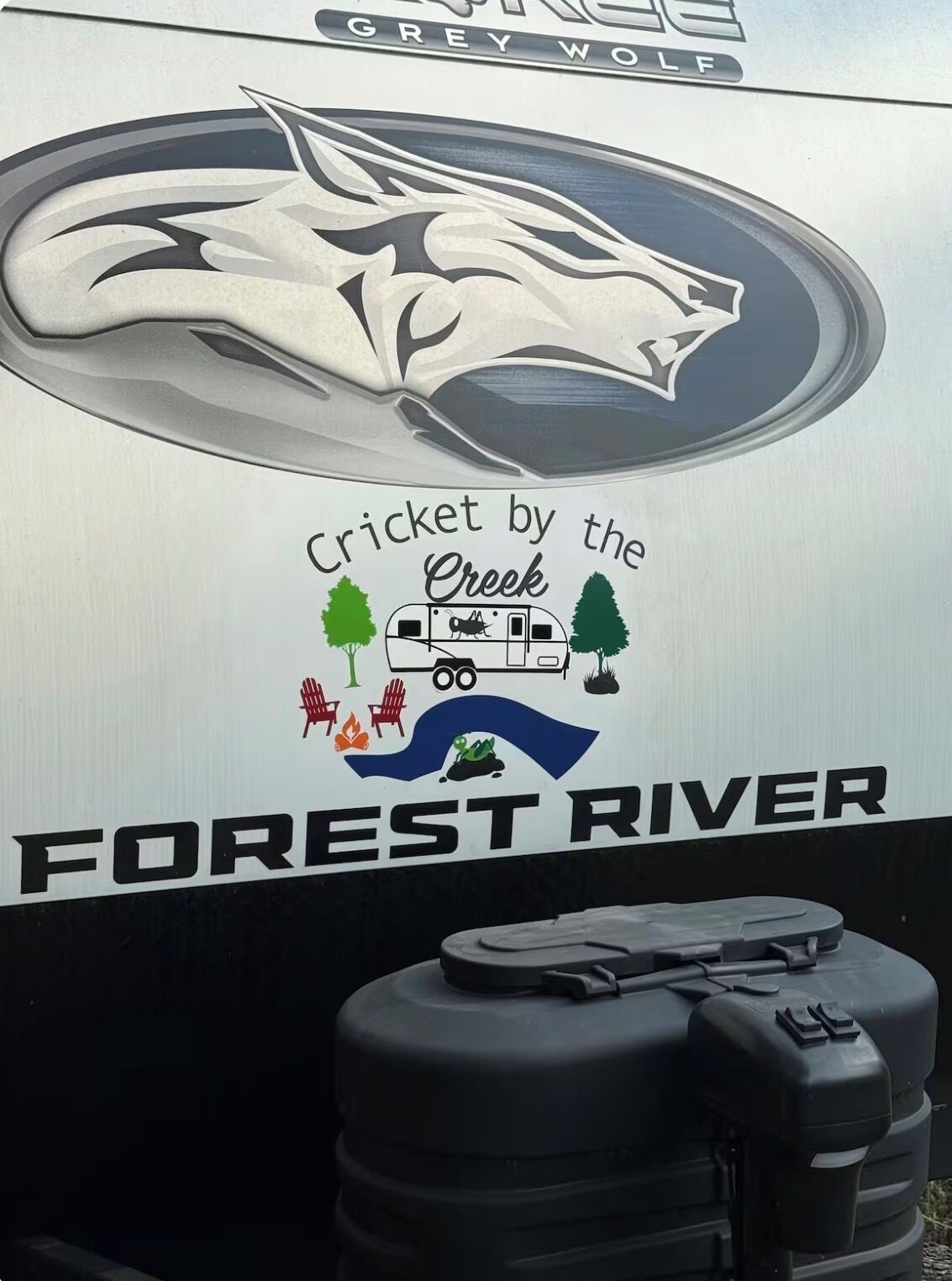 Ein Wohnmobil mit dem Schriftzug 'Cricket by the Creek' und 'Forest River'.