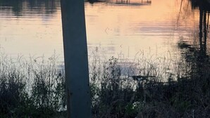 Eine Brücke über ruhigem Gewässer mit einem Steg und einem kleinen Gebäude am gegenüberliegenden Ufer.