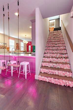 Eine Treppe mit pinkfarbener Blütenoptik, ein Küchenbereich mit Bar und ein Sitzbereich mit Schaukeln.