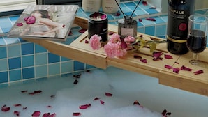 A bathroom with a bathtub filled with rose petals, a magazine, a bottle of shampoo, a bottle of perfume, a bottle of wine, and a glass. - Aries Boutique Hotel Vung Tau (Ho Chi Minh City)