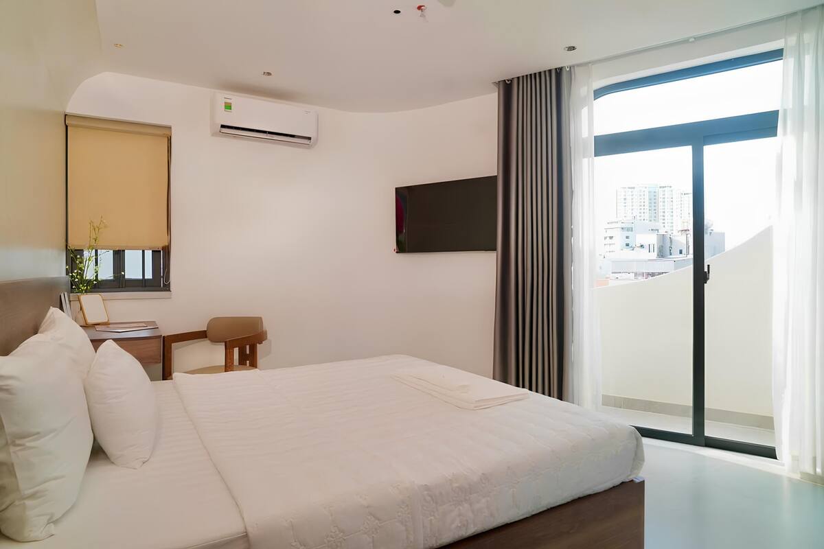 Una camera d'albergo con un letto, una scrivania, una sedia, una televisione e un'ampia finestra.