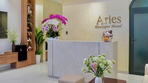 Uma área de recepção de hotel com um balcão de mármore, uma estante de madeira e uma placa na parede para o 'Aries Boutique Hotel'.