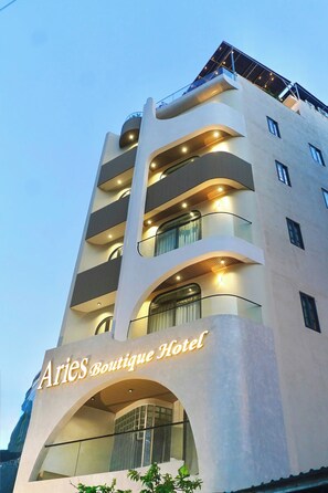 Monikerroksinen hotelli, jossa on parvekkeet, huomiota herättävä kaareva sisäänkäynti ja nimikyltti, jossa lukee: »Aries Boutique Hotel».