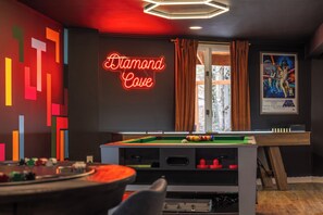 A pool table with a neon sign reading 'Diamond Cove,' a Star Wars poster, and a colorful geometric wall design.