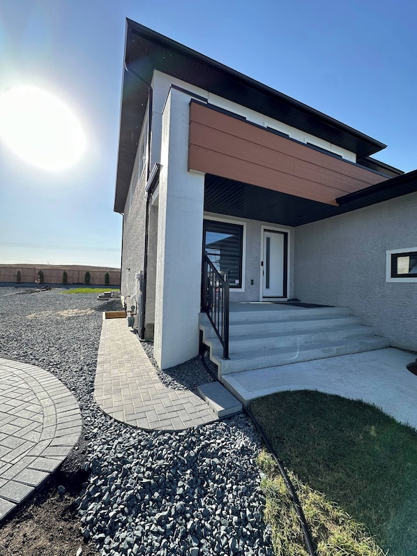 Une maison moderne à deux étages, dotée d’un porche couvert, d’une allée bordée de pierres et d’une pelouse.