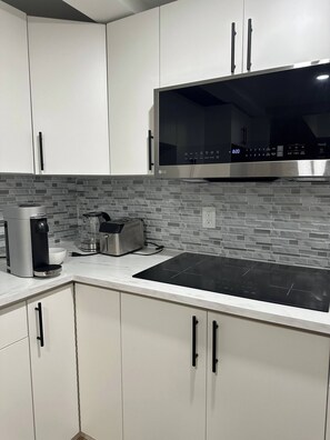 A modern kitchen with white cabinets, a black induction cooktop, a coffee maker, and a toaster.