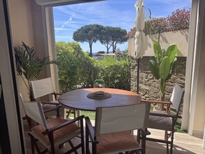 Ein runder Holztisch mit vier Stühlen, einer Glaseinfriedung und Blick auf einen Garten mit Bäumen und einer Steinmauer.