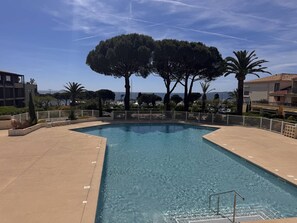 Une piscine offrant une vue dégagée sur la mer, entourée d’arbres et de bâtiments.