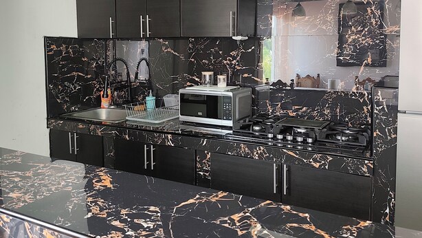Cocina moderna con armarios oscuros, encimera de mármol negro, microondas, estufa e iluminación colgante.