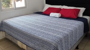 Un dormitorio con una cama, una ventana con cortinas, un equipo de aire acondicionado y dos cuadros colgados en la pared.