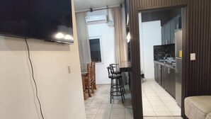 Una sala moderna con un televisor de pantalla plana, un comedor con sillas, una cocina con armarios y un sofá.
