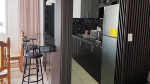 Una cocina moderna con gabinetes negros, encimera de mármol y horno empotrado. Hay un comedor con mesa de madera y taburetes negros.