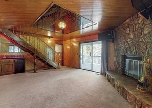 A spacious room with a stone fireplace, a wooden staircase, and a large window.