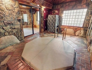A spa area with a stone wall, a glass door leading outside, and a large, cushioned hot tub.