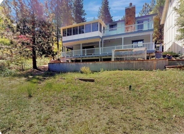 A two-story house with a balcony, surrounded by a grassy yard and trees.