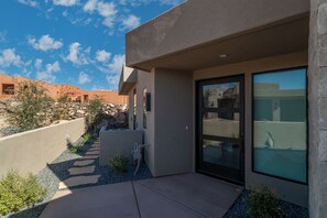 A modern building with a stone facade, a glass door, and a small garden area with rocks and plants.