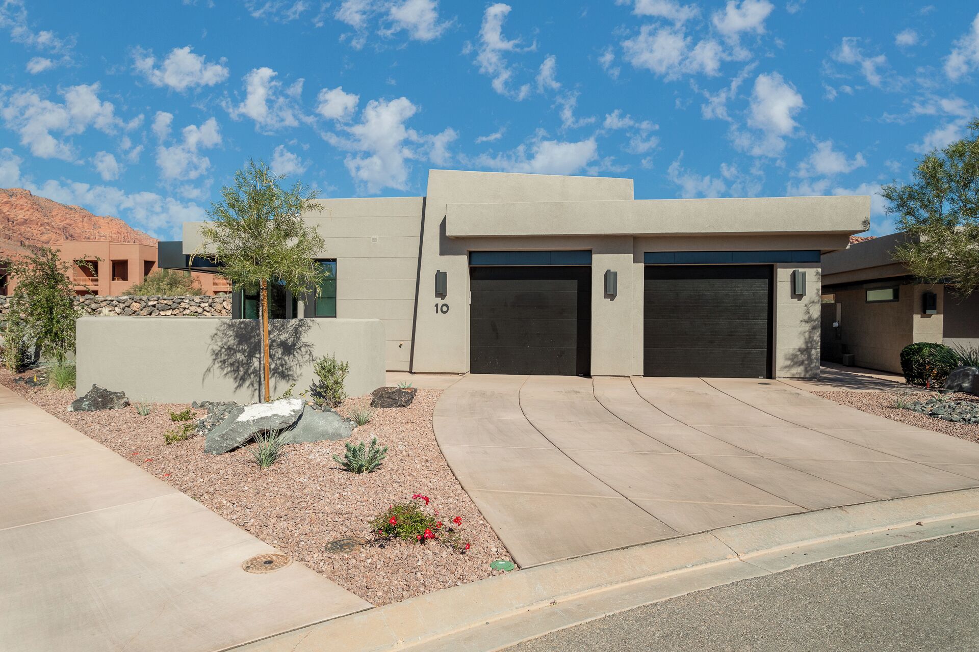 A modern two-story house with a garage, a stone wall, and a landscaped garden.