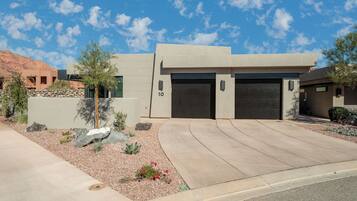 A modern two-story house with a garage, a stone wall, and a landscaped garden.