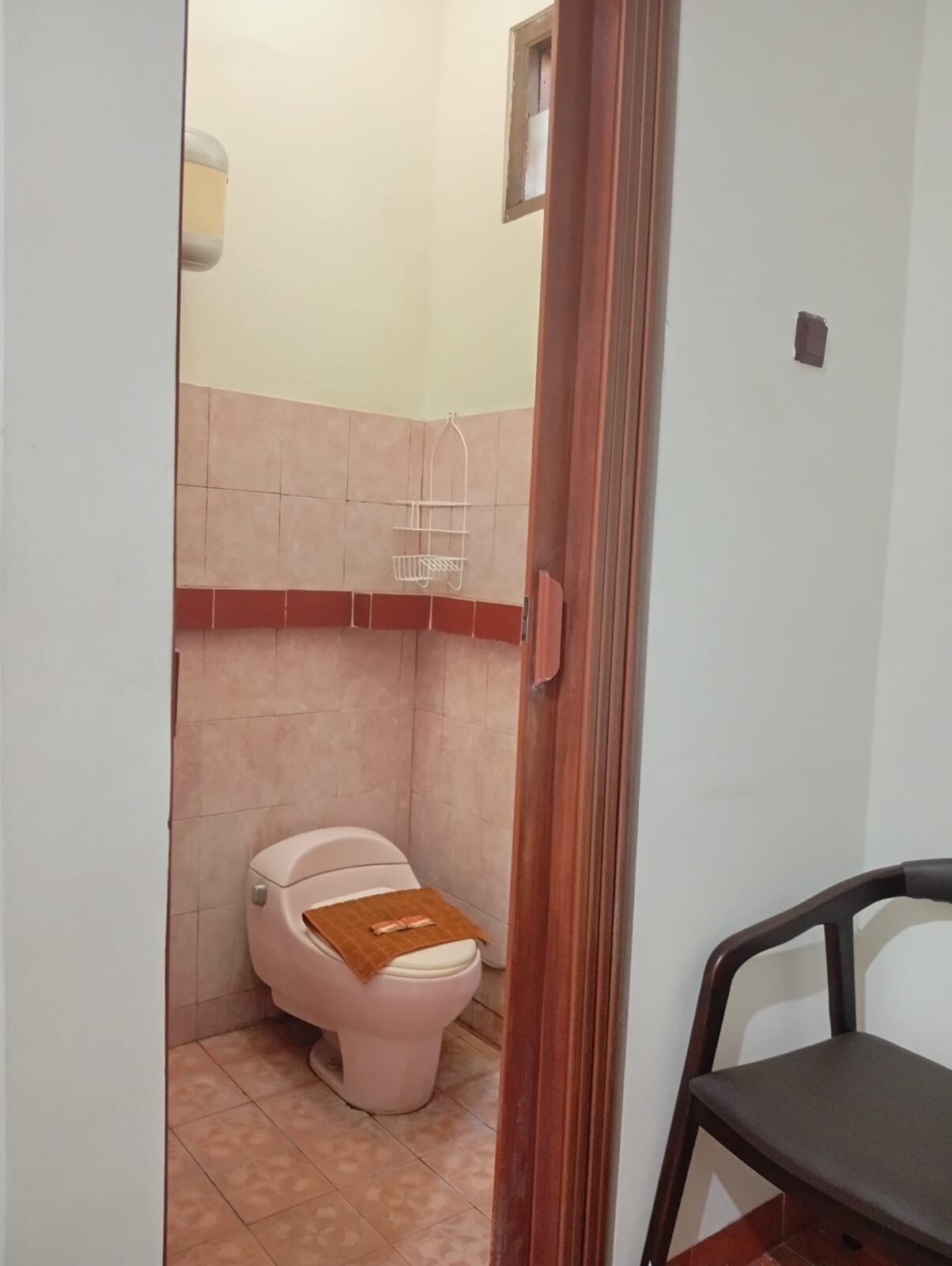 A small bathroom with a toilet, a shower area, and a chair.