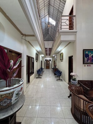 Un pasillo de hotel con techo alto, un ventilador de techo y una larga fila de sillas azules.