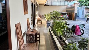 Un pasillo cubierto con piso de baldosas, sillas de madera, una mesa y plantas en macetas.