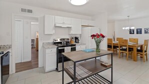 Una cocina moderna con armarios blancos, una estufa y un comedor con sillas y mesa de madera.