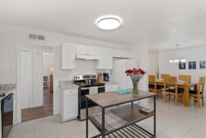 Une cuisine moderne avec des meubles blancs, une cuisinière et un coin repas comprenant des chaises et une table en bois.