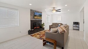 Una sala de estar con chimenea, un sofá, un ventilador de techo y un mueble para televisión.