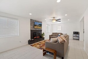 Un salon avec une cheminée, un canapé, un ventilateur de plafond et un meuble pour la télévision.