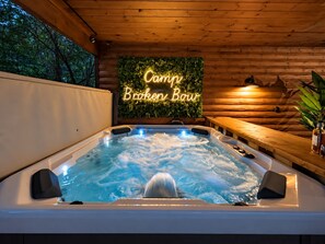 Ein Whirlpool mit einem Neon-Schild, auf dem 'Camp Broken Bow' steht, in einer Holzhütte.