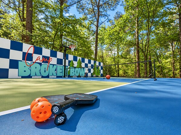 Ein Basketballplatz im Freien mit einer Schachbrettwand und Bäumen im Hintergrund.