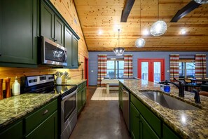 A kitchen with green cabinets, a stainless steel microwave, and a granite countertop. - Camp Broken Bow - Pickleball, Arcade & Hot Tub · Private Resort for Groups (Broken Bow)