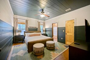 Ein Schlafzimmer mit einem Bett, zwei Poufs, einem Deckenventilator und einer Tür.