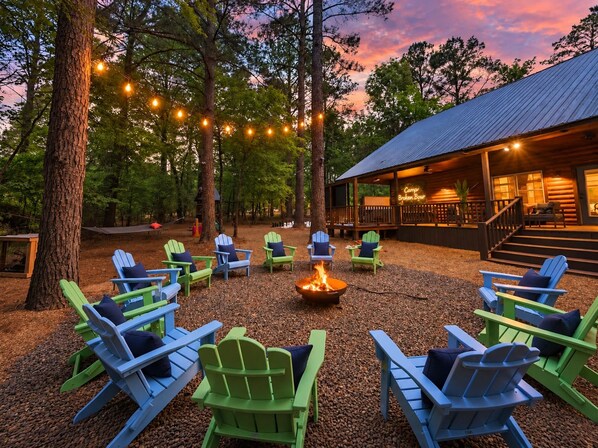 A camp with outdoor seating and a fire pit surrounded by trees. - Camp Broken Bow - Pickleball, Arcade & Hot Tub · Private Resort for Groups (Broken Bow)