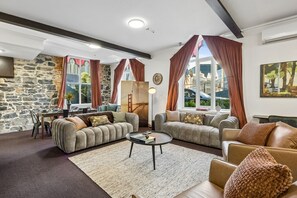 A living room with a stone wall, two sofas, a coffee table, and a dining area with a table and chairs. - Chapel on Moray, historical significance with modern luxury. (Dunedin)