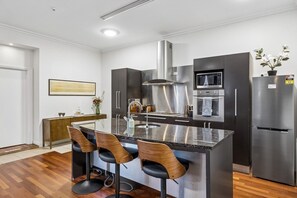 A modern kitchen with a central island, bar stools, stainless steel appliances, and a wooden sideboard. - Chapel on Moray, historical significance with modern luxury. (Dunedin)
