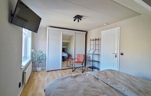 Un dormitorio con cama, televisión, ventilador de techo, puerta corredera y ventana.