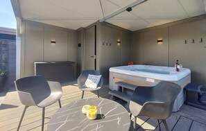 Un espacio al aire libre techado con jacuzzi, dos sillones y una mesa con una botella y vasos.