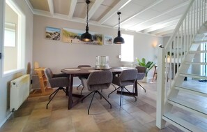 Un comedor con una mesa redonda, sillas grises, lámparas colgantes y obras de arte en la pared.