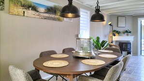 Uma sala de jantar com uma mesa redonda, seis cadeiras, duas luminárias pendentes, um vaso de vidro e um quadro na parede.
