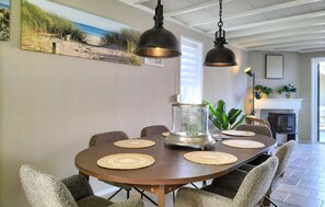 A dining area with a round table, six chairs, two pendant lights, a glass vase, and a painting on the wall. - Amazing home in Stavenisse with swimming pool (Stavenisse)