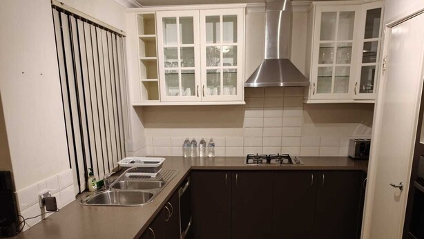 A kitchen with a central island, dark cabinets, white upper cabinets, a stainless steel range hood, and a tiled floor. - Airport  3-bedroom villa with AC in charming High Wycombe (High Wycombe)
