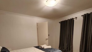 A hotel room with a bed, a bedside table, a mirror, a window with curtains, and a carpeted floor. - Airport  3-bedroom villa with AC in charming High Wycombe (High Wycombe)