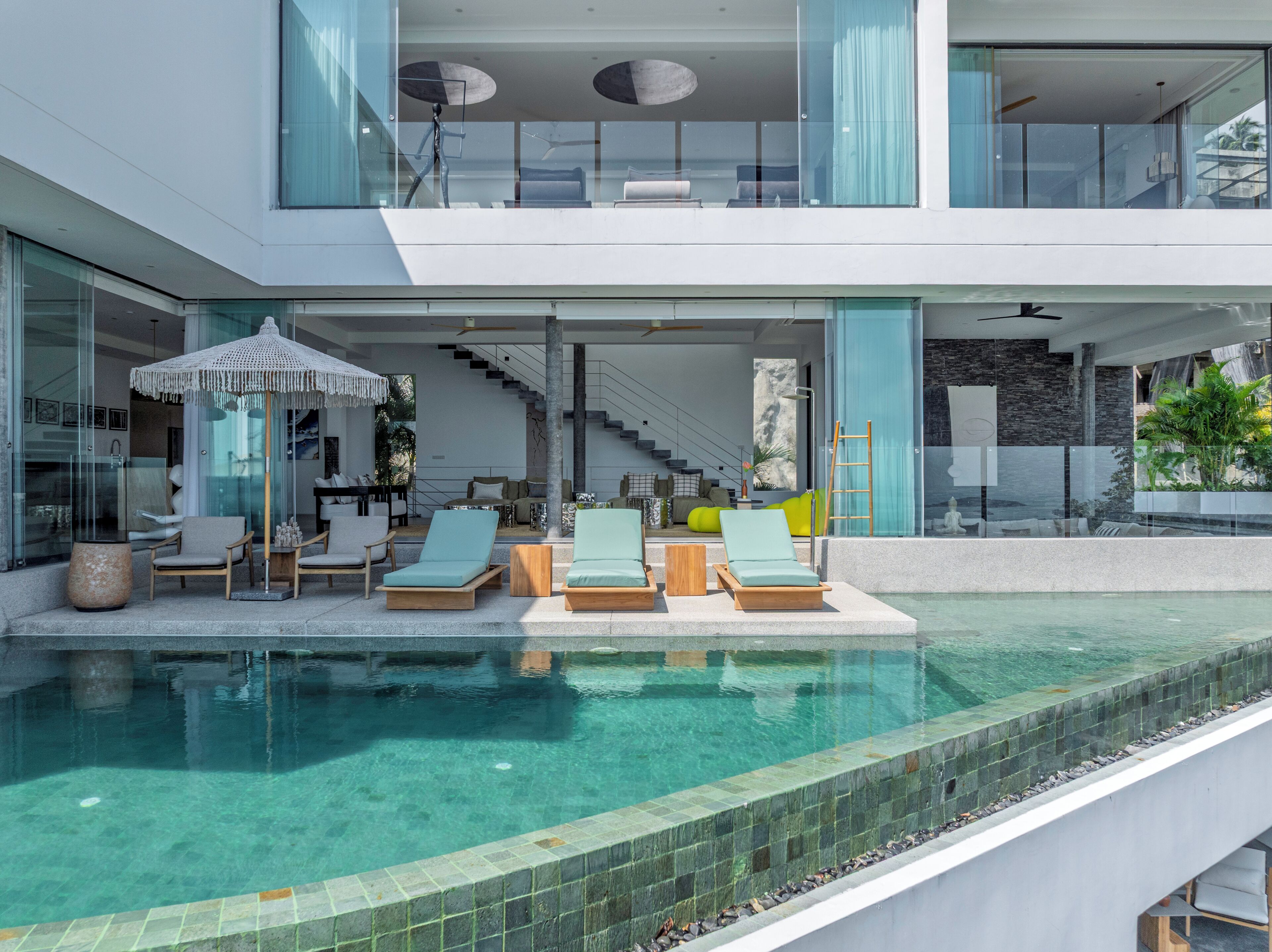 A modern house with a swimming pool, outdoor seating, and a staircase leading to an upper level.