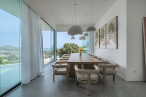 A modern dining room with a long table, chairs, and a view of the outdoors. - Villa Vie (Koh Samui)