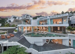 Une maison moderne à plusieurs étages, dotée d’une piscine centrale, d’un espace salon extérieur et d’un escalier menant aux niveaux supérieurs.